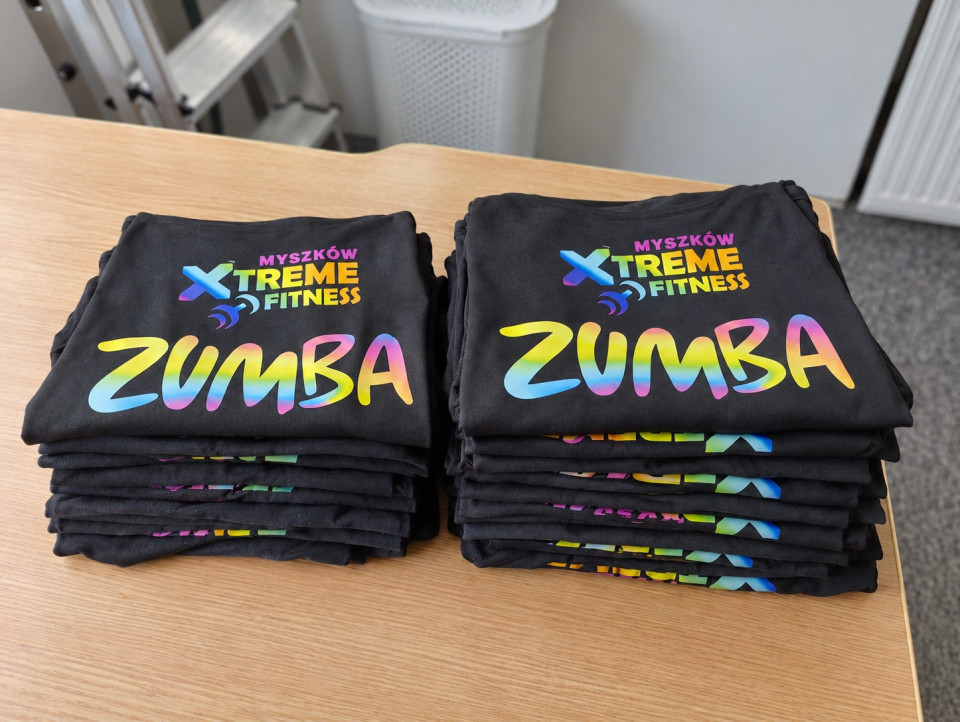 Stosy czarnych koszulek z kolorowym nadrukiem ZUMBA i logo klubu